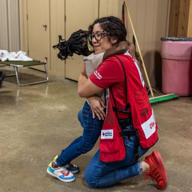 A Red Cross volunteer hugging a child.