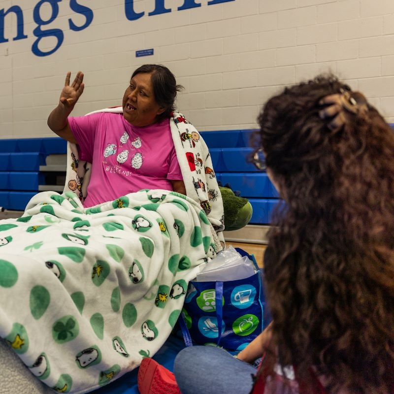 Aurora Ramirez sitting on a cot talking in a Red Cross shelter.
