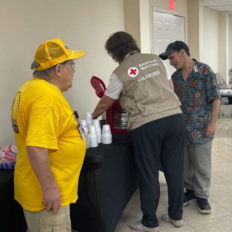 Three Red Cross volunteers standing by a coffee station.