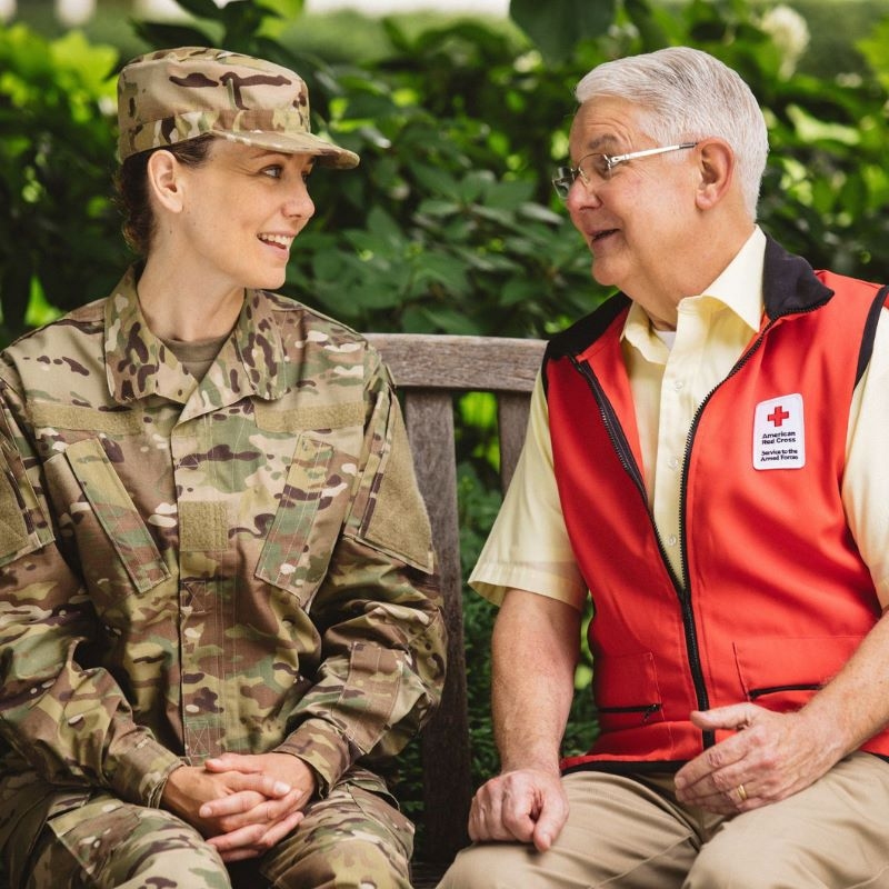 Red Cross volunteer sitting next to service member in uniform.