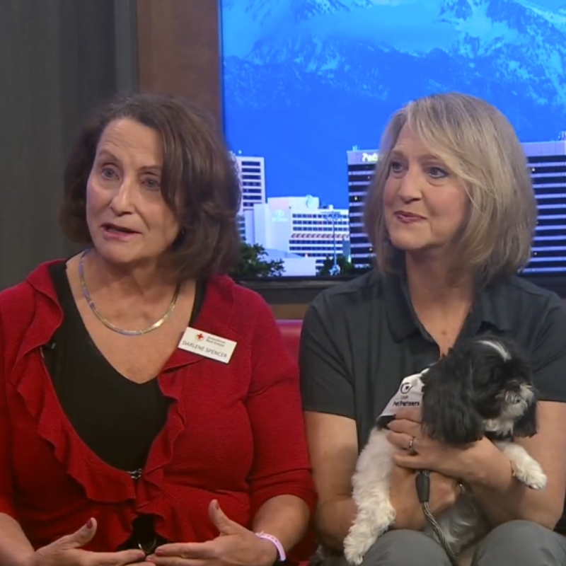 Two women sitting on a couch with a dog on their lap.