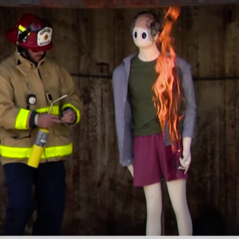 Firefighter standing next to a mannequin that is on fire. 