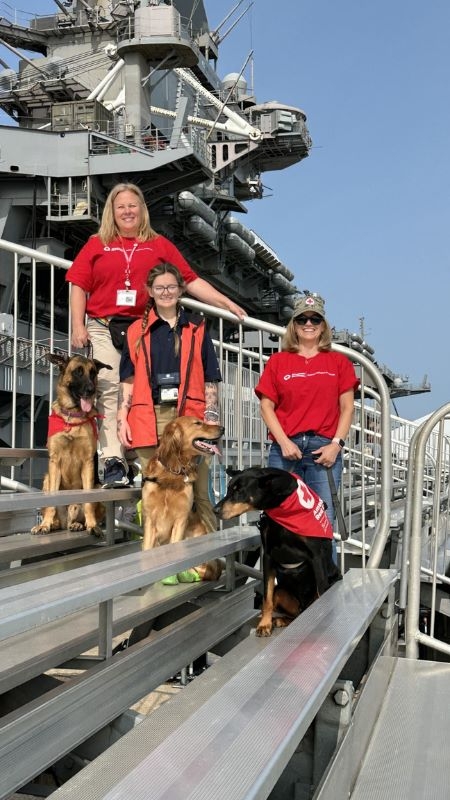Three Red Cross volunteers with three dogs on the USS Truman.