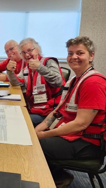 Three Red Cross volunteers sitting a table giving the thumbs up.