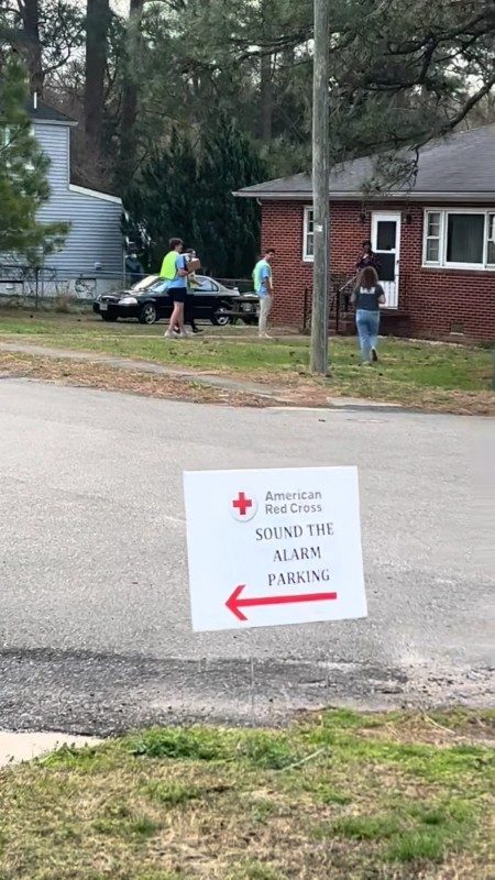 Three Red Cross volunteers walking up to a home with "Sound the Alarm parking" sign in front yard.