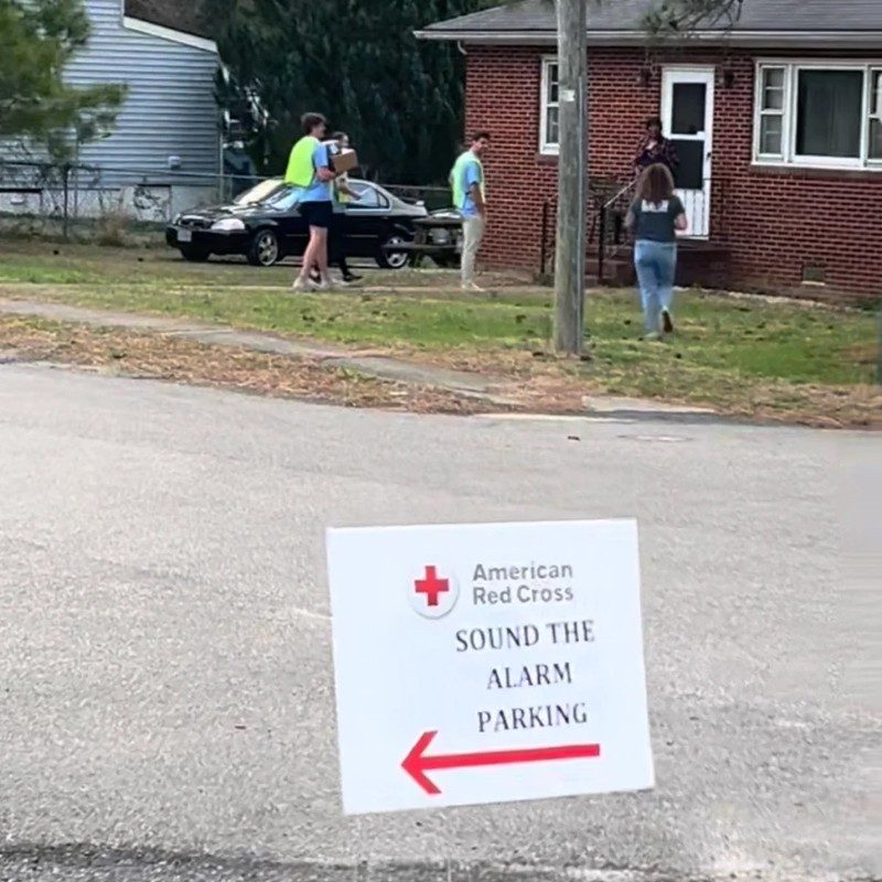 Three Red Cross volunteers walking up to a home with "Sound the Alarm parking" sign in front yard.