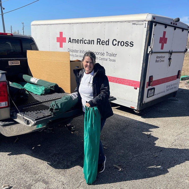 a woman loading the back of a truck next to a Red Cross trailer.