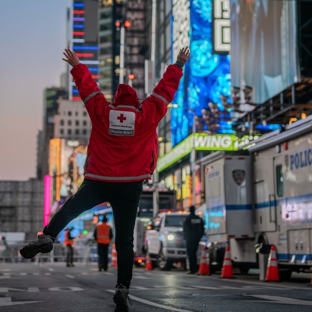 red cross volunteer gleefully jumping mid air in times square.