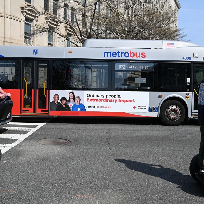 A bus with a Red Cross ad driving on the road.