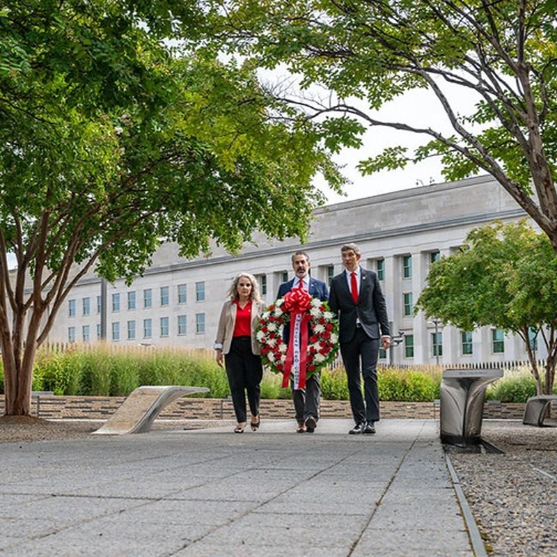 Three people carrying a large wreath.