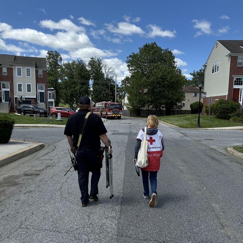 A Red Cross volunteer and a firefighter walking down the road.