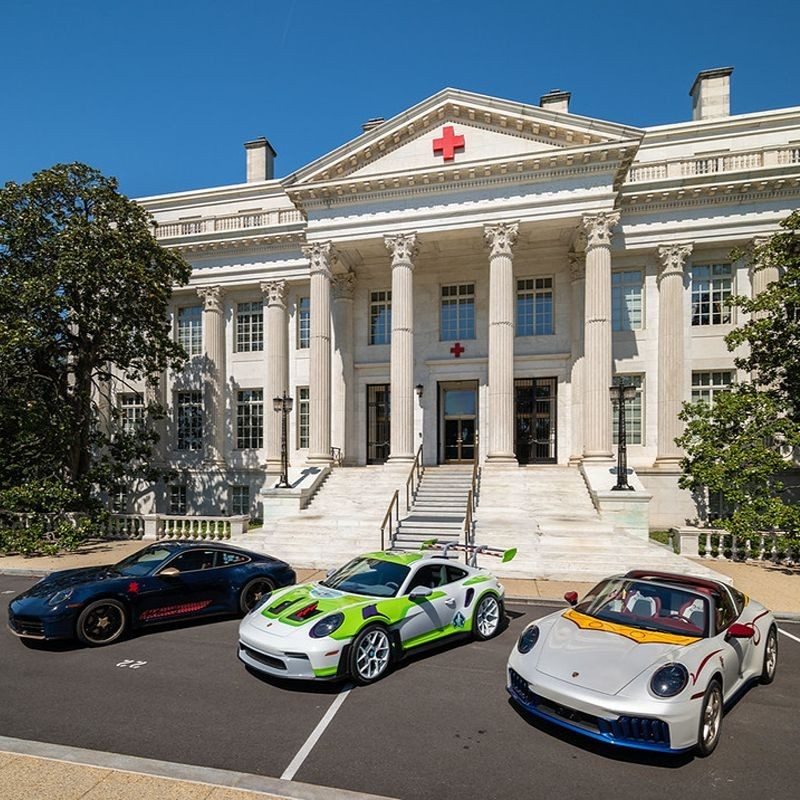 Three Porsches in front of a Red CRoss building.