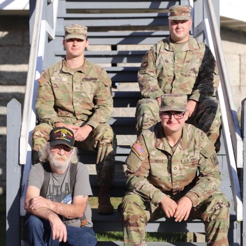Three men in military uniforms next to a man in a gray shirt.
