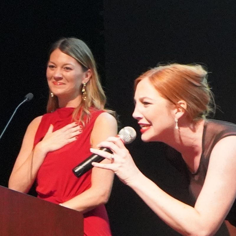 Two women at a podium with one holding a mic.