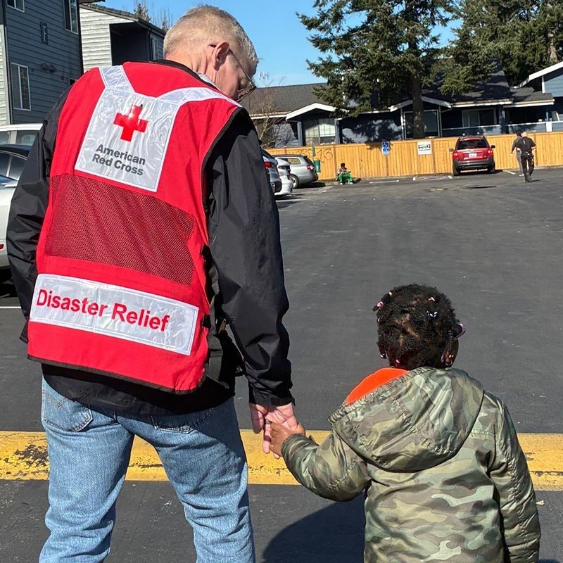 A Red Cross volunteer holding a child's hand walking across the street.
