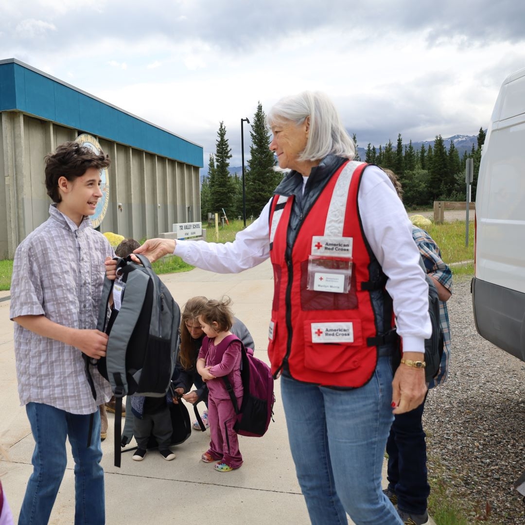 woman handing backpack to boy