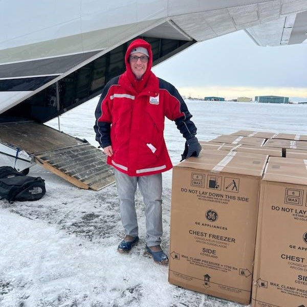 Red Cross volunteer standing next to large boxes and a cargo plane in the snow.