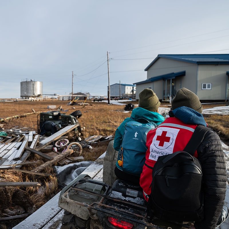 Two Red Cross volunteers on a 4 wheeler with debris scattered around them.