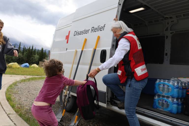 Red Cross volunteer hands young child backpack