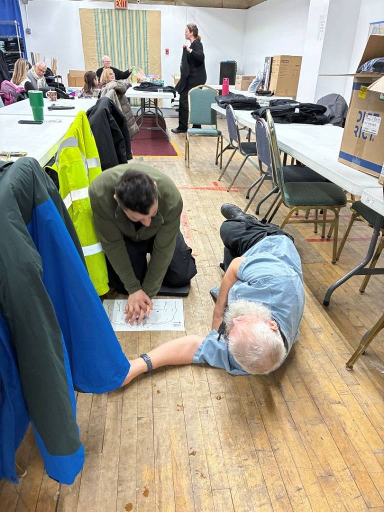Man practices chest compressions while another man lays nearby