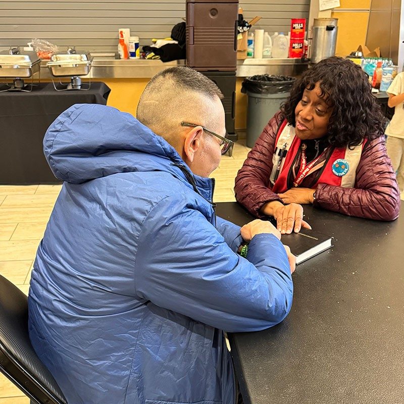 Kipnuk resident sitting at a table with a Red Cross volunteer with both of their hands on a Yup’ik bible.
