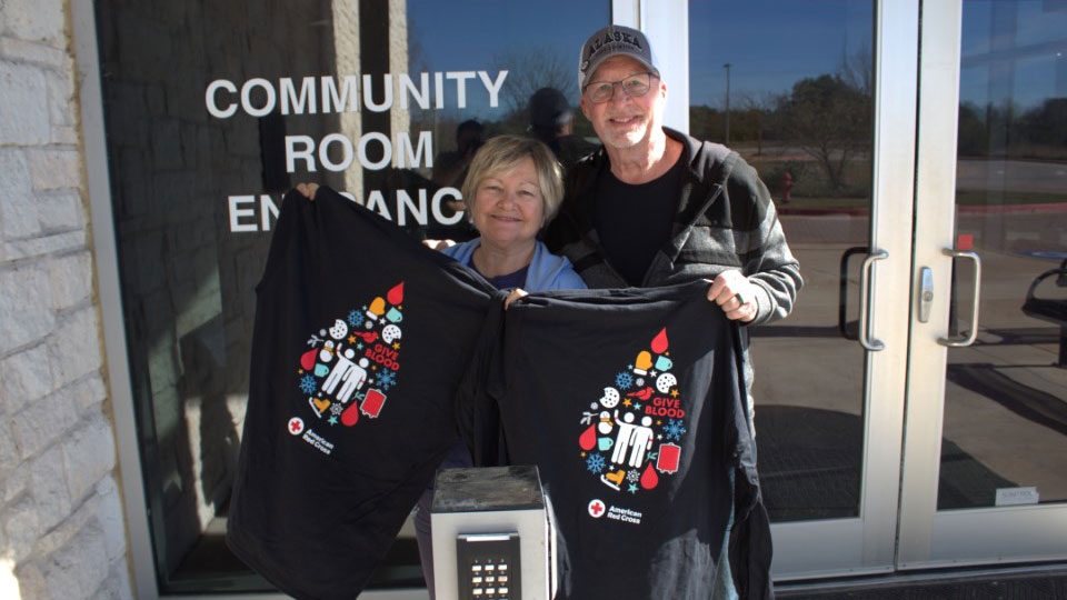 Man and woman stand holding blood donor shirts.