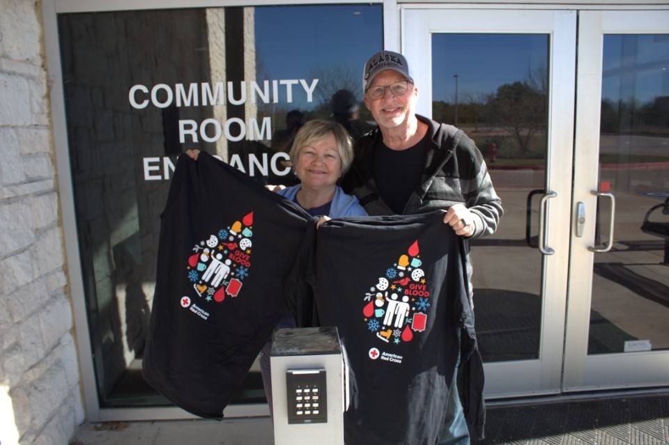 Man and woman stand holding blood donor shirts