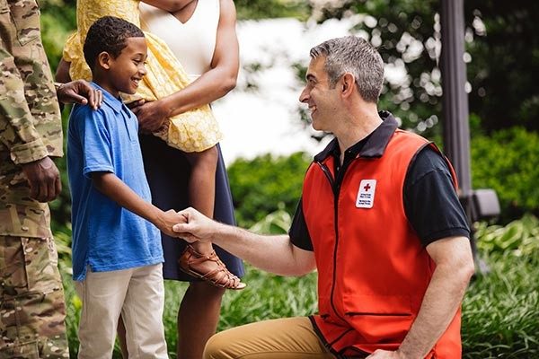 Red Cross volunteer kneeling down and shaking hands with youngster.