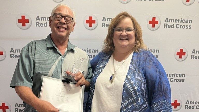 Vic Moulakis standing next to a woman while holding a Red Cross award at a Red Cross event.
