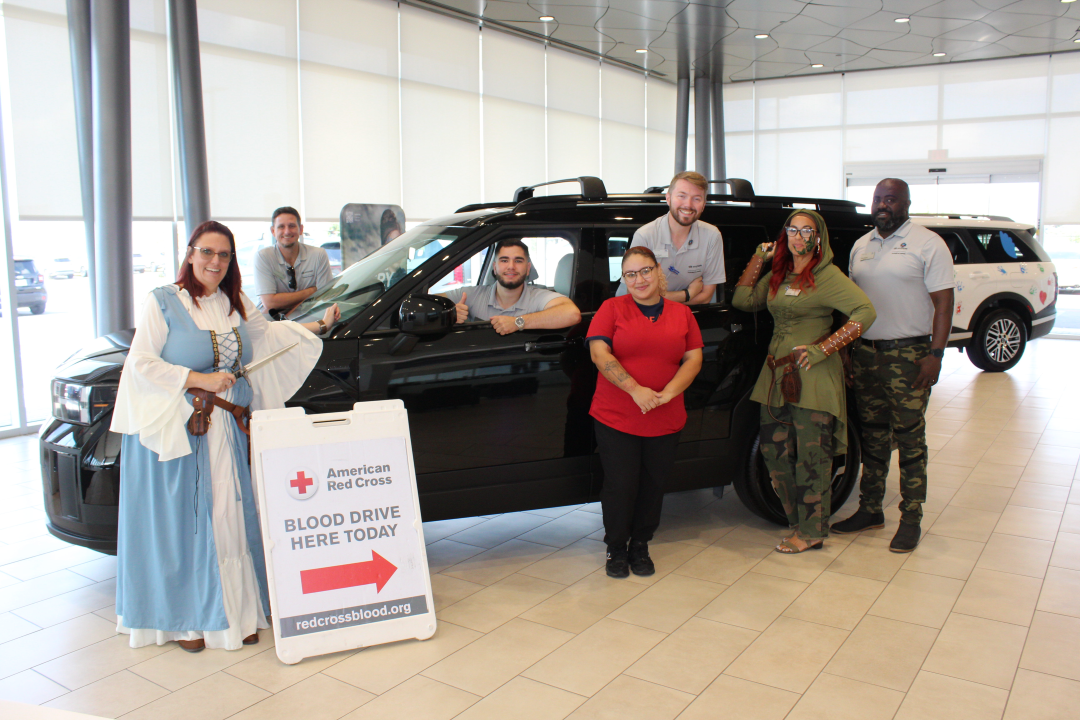 People stand around car in front office space of car dealership