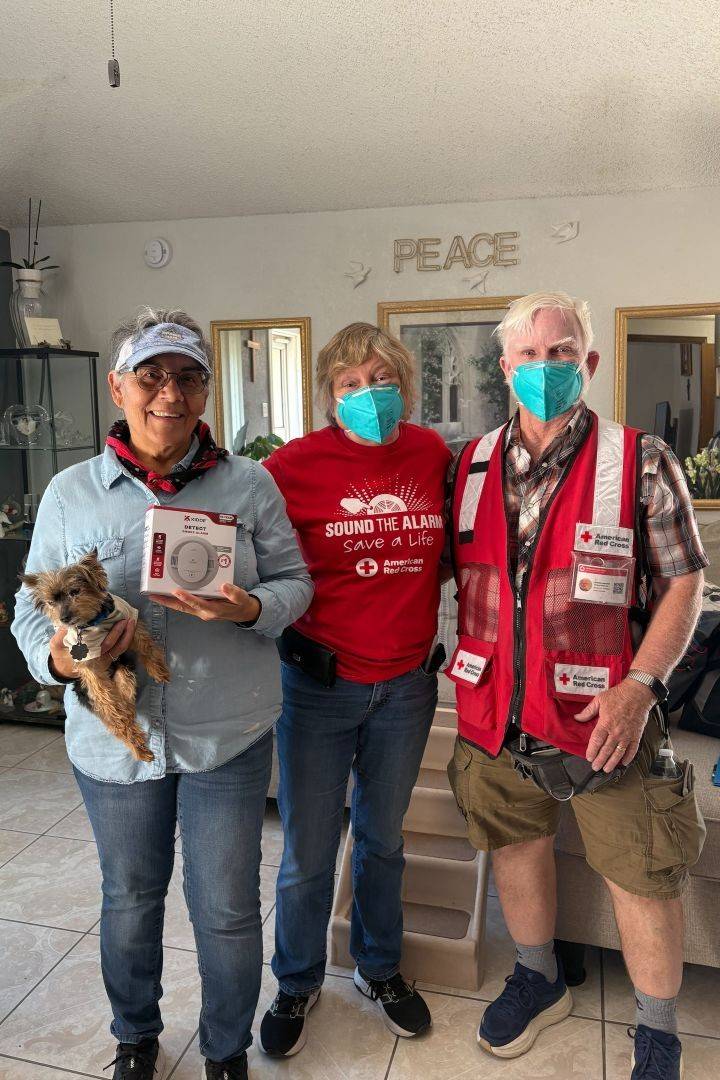Two red cross volunteers stand inside home with owner during smoke alarm install