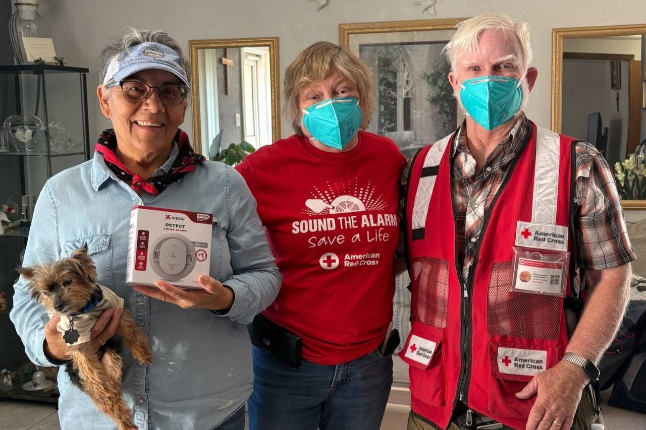 Two red cross volunteers stand inside home with owner during smoke alarm install