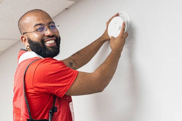 Red Cross volunteer installing a smoke alarm on a wall.