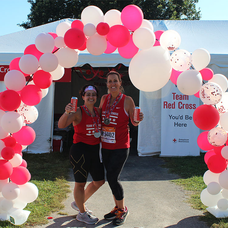 Two marathon runners under pink and white ballon arch holding drinks and smiling 