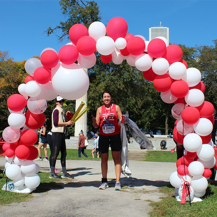 Marathon runner under pink and white ballon arch holding drink and smiling