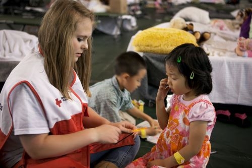 red cross volunteer playing with two children in a shelther 