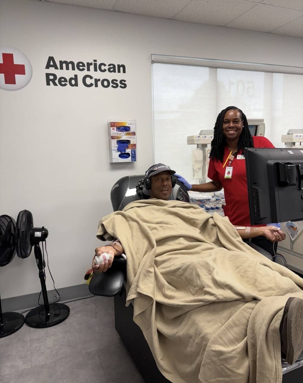 Man sits under blanket with headphones on in blood donation chair
