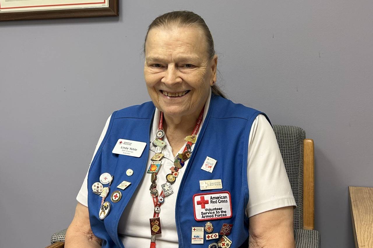 Woman sits wearign vest with Red Cross logo and pins