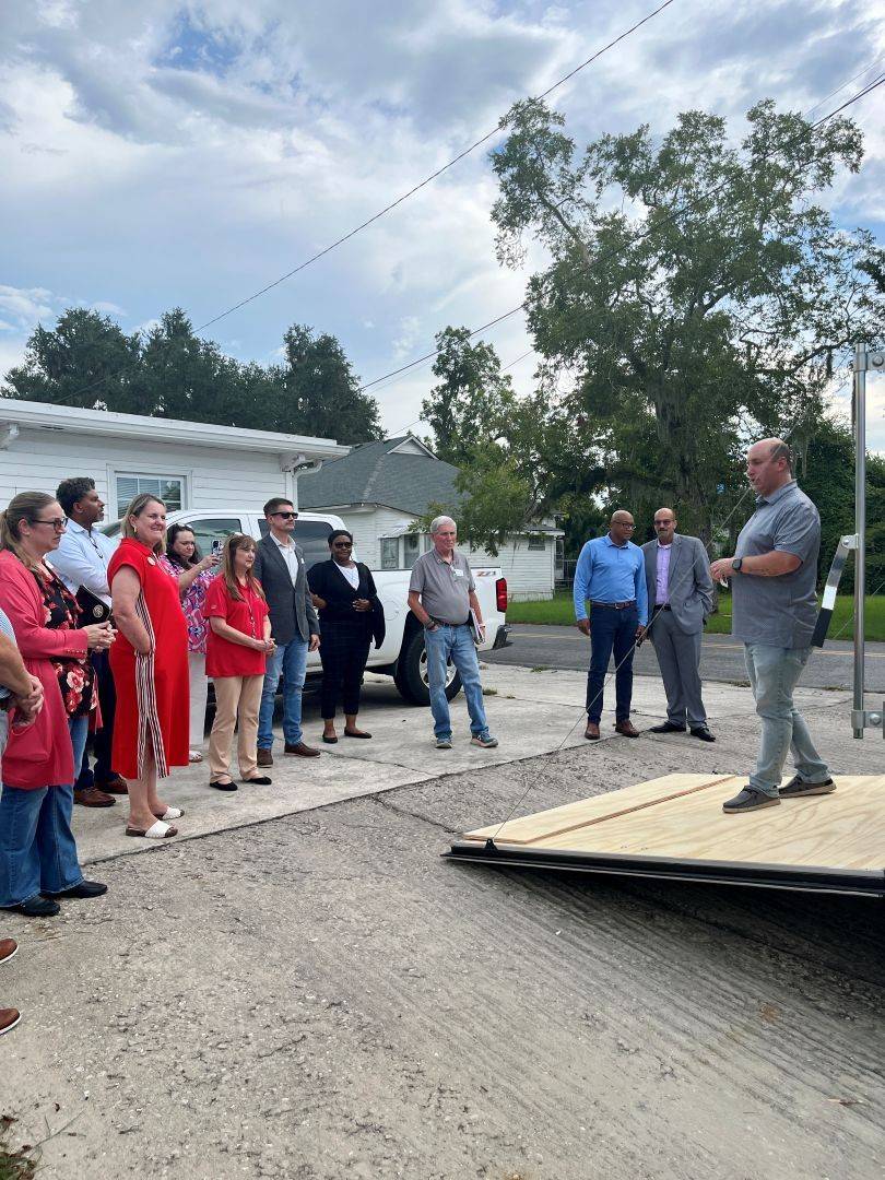 Man stands on open trailer talking to group of people