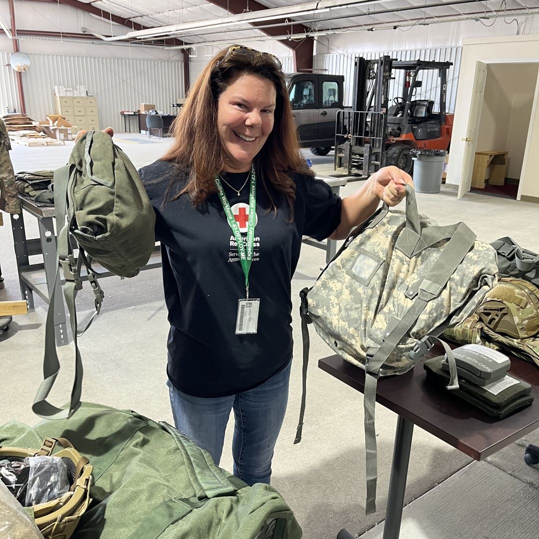 woman in red cross shirt holds military style bags