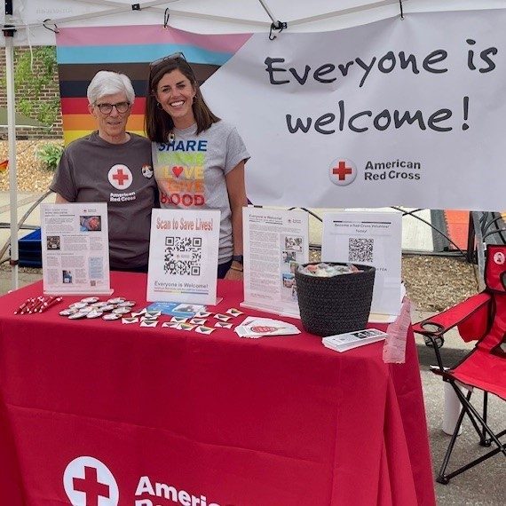 two women stand behind table in pride shirts