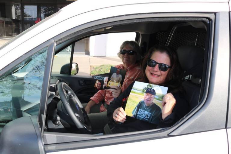 Two women hold photos of Mario Hollis while sitting in blood transport vehicle. 