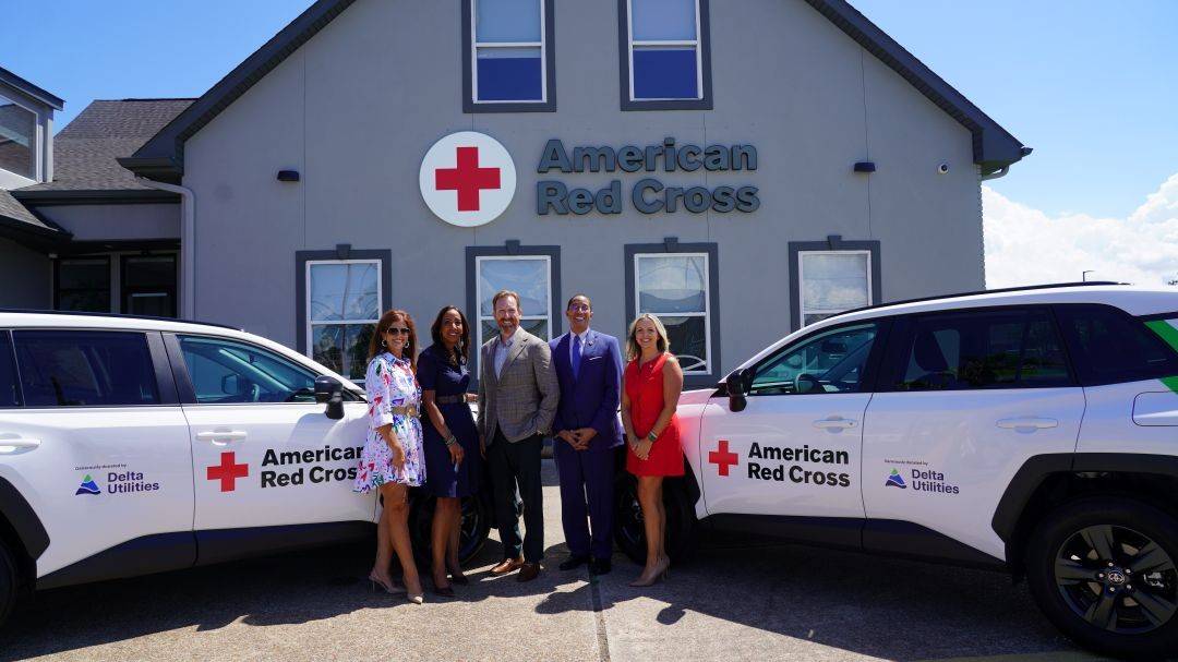 Group of people stand between two Red Cross hybrid vehicles