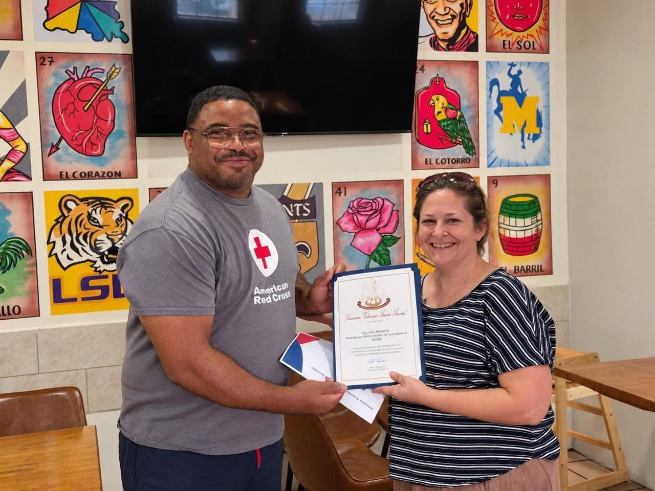 Man in Red Cross tshirt stands holding award with woman