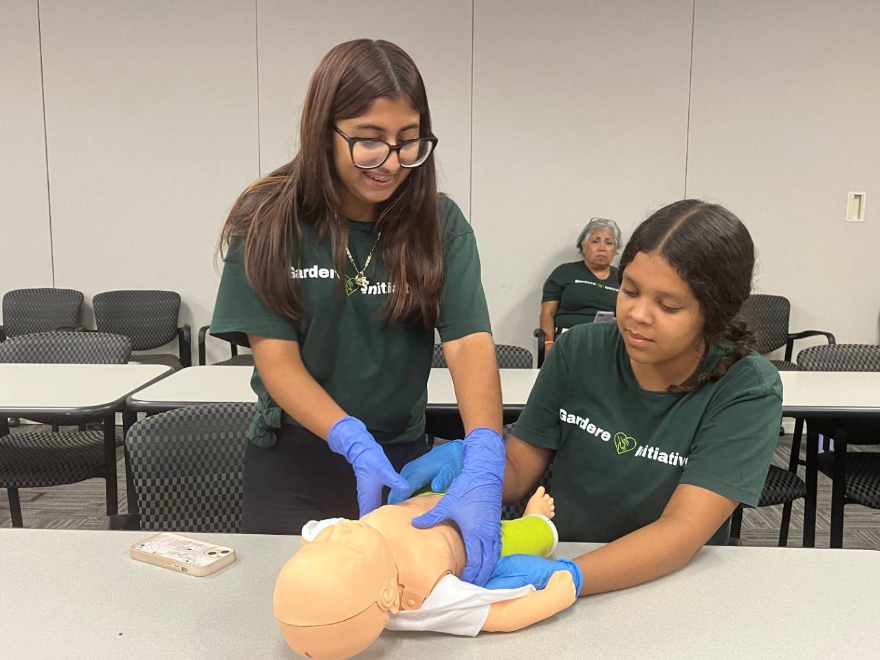 Two youth practice CPR on child CPR mannequin