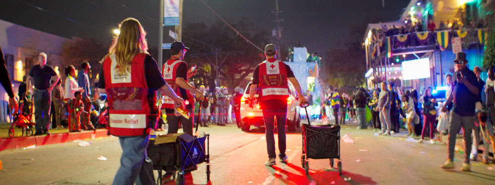 red cross volunteers pushing carts in the street at a mardi gras parade.