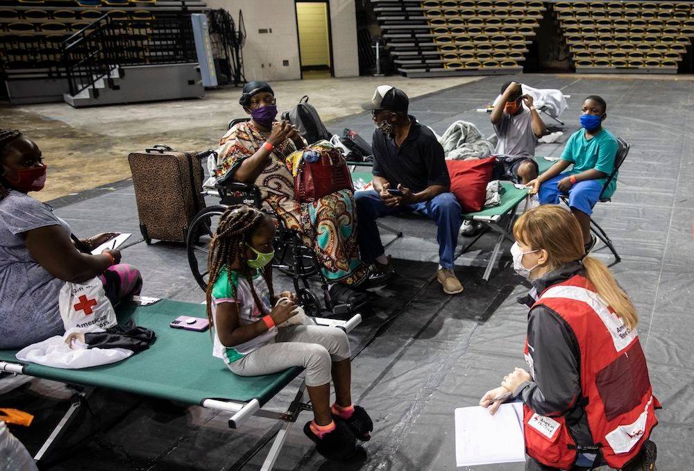 August 29, 2021. Baton Rouge, Louisiana. Wendy Halsey of the American Red Cross visits Moriah Killingsworth of Baton Rouge, with her extended family in background at a Red Cross evacuation center on Sunday August 29, 2021. The family is among those seeking refuge from Hurricane Ida. As they prepare to wait out the storm, the family chats and laughs together and remains upbeat. Across Louisiana and Mississippi, the Red Cross and other organizations have opened dozens of evacuation shelters, offering safe refuge for hundreds of people. The number of open shelters and people staying in them is changing hourly. Photo by Scott Dalton/American Red Cross