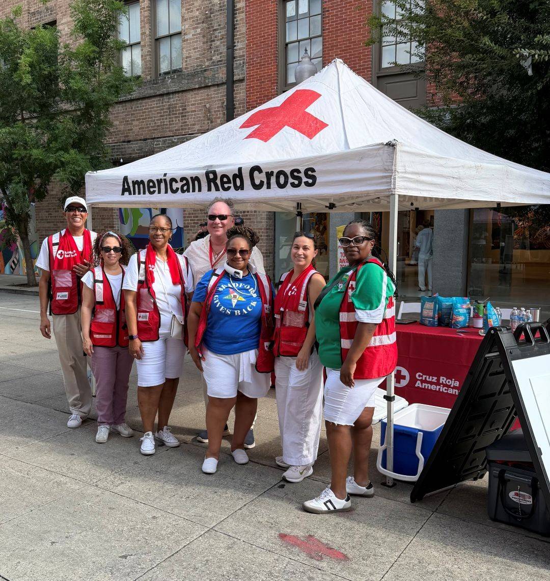 Group of Red Cross volunteers stand in front of Red Cross tent