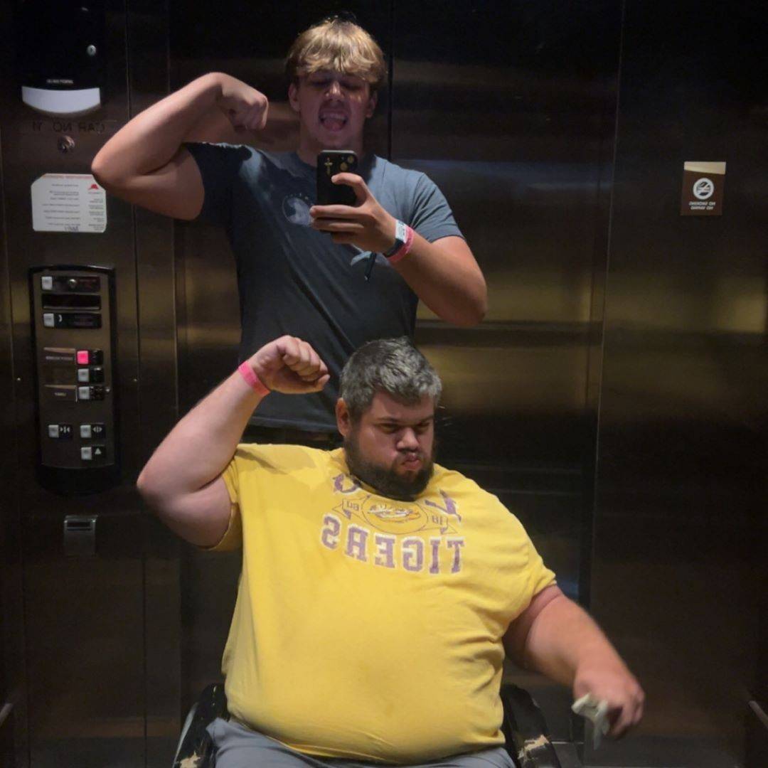 Man sits in front of younger man and both hold up strong arm pose
