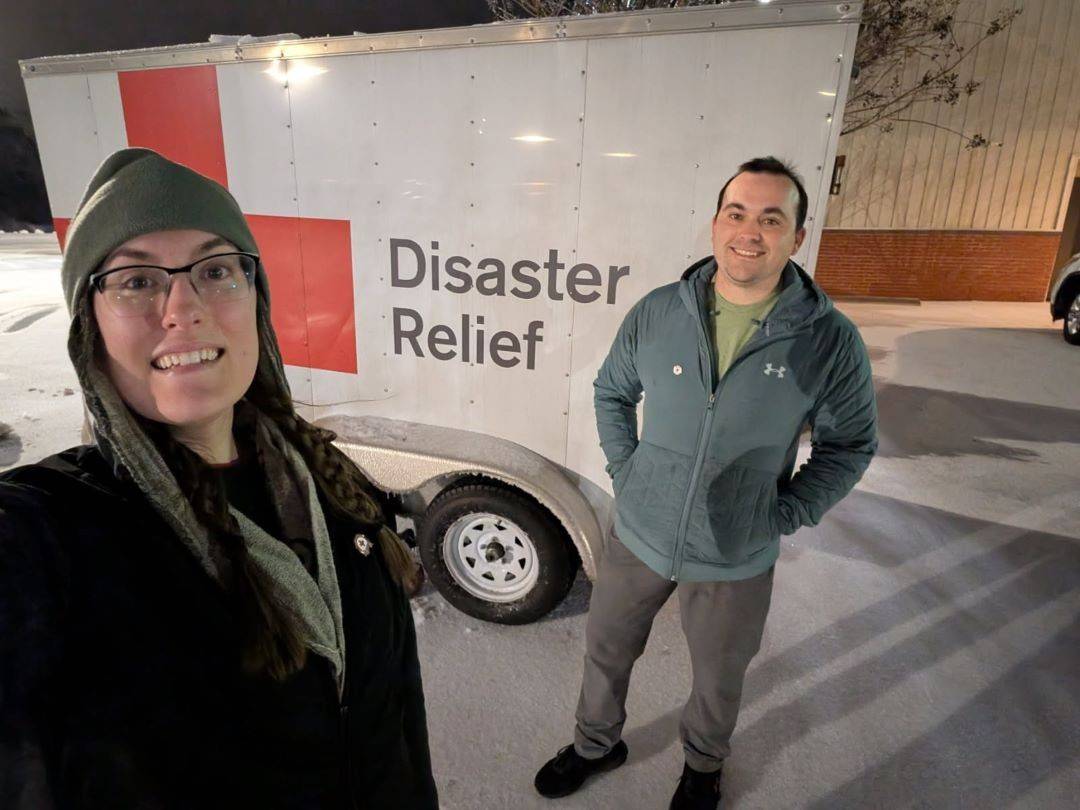 Man and woman stand in front of Red Cross trailer